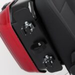 Close-up van een rode motorzij-koffer met bevestigingsbeugels en klittenband naast het zadel.