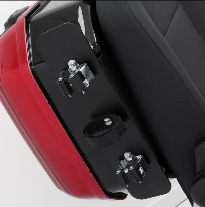 Close-up van een rode motorzij-koffer met bevestigingsbeugels en klittenband naast het zadel.