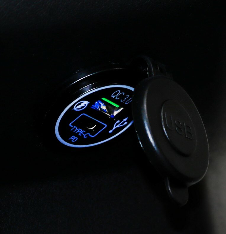 Close-up van een verlichte USB-A en USB-C (PD) oplaadpoort met open rubberen afdekdop.