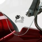 Close-up van gehard windscherm met E24-keurmerk en metalen bevestiging op rode scooter.