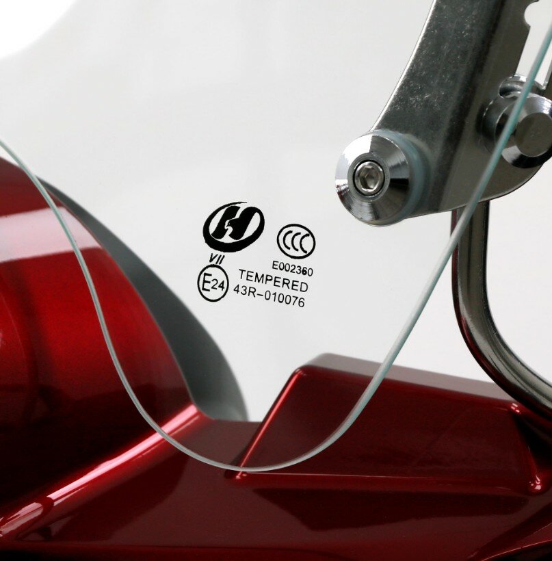 Close-up van gehard windscherm met E24-keurmerk en metalen bevestiging op rode scooter.
