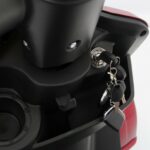 Close-up van het contactslot van een scooter met sleutelbos en zwart paneel.