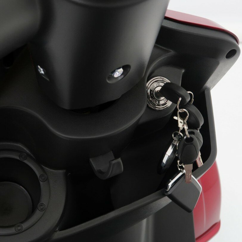 Close-up van het contactslot van een scooter met sleutelbos en zwart paneel.