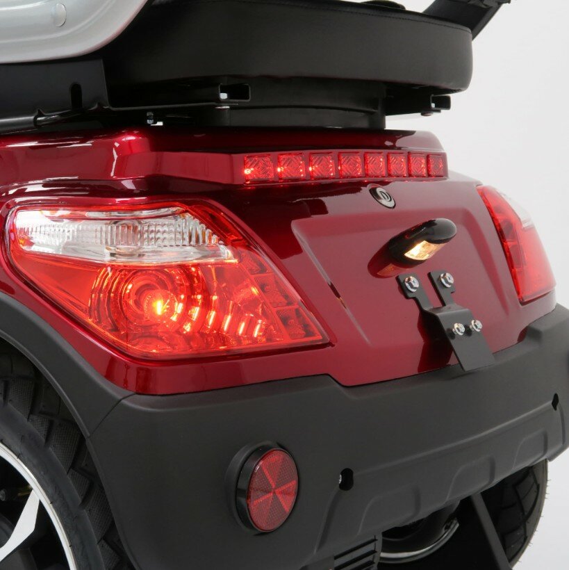 Close-up van de achterzijde van een rode scootmobiel met brandende achterlichten, LED-strook en reflector.