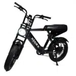 Zwarte mopedstijl e-bike met dikke banden, brandende ronde koplamp en lang zadel op witte achtergrond.