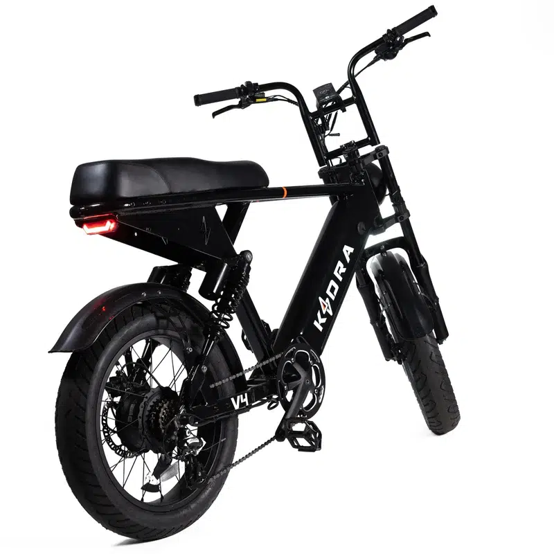 Zwarte e-bike met moped-stijl, brede banden, lang zadel en achterlicht, schuin van achteren gezien.