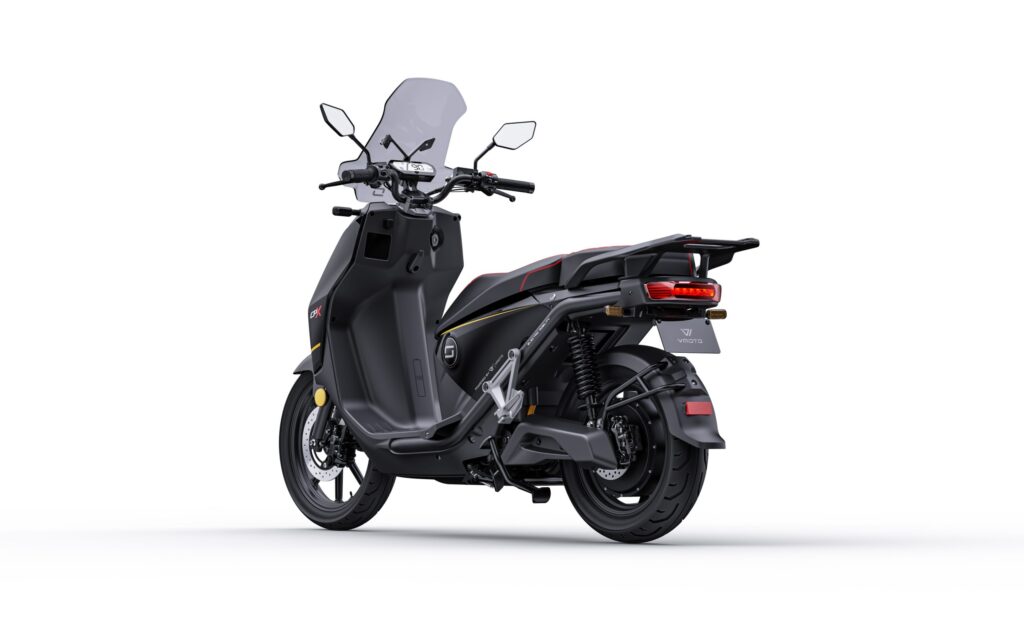 Zwarte elektrische scooter met windscherm en bagagedrager, schuin van achter op witte achtergrond.