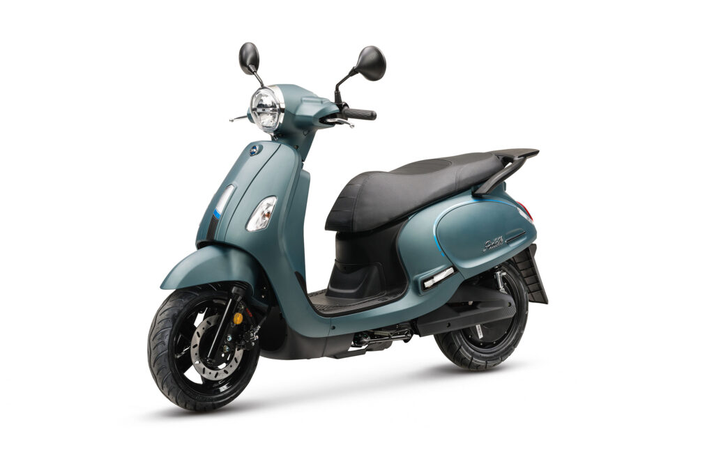 Groenblauwe retro-scooter schuin van voren, met ronde koplamp, zwarte zitting en spiegels op witte achtergrond.