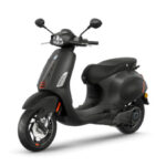 Mat zwarte scooter met oranje accenten, driekwartsaanzicht tegen witte achtergrond.