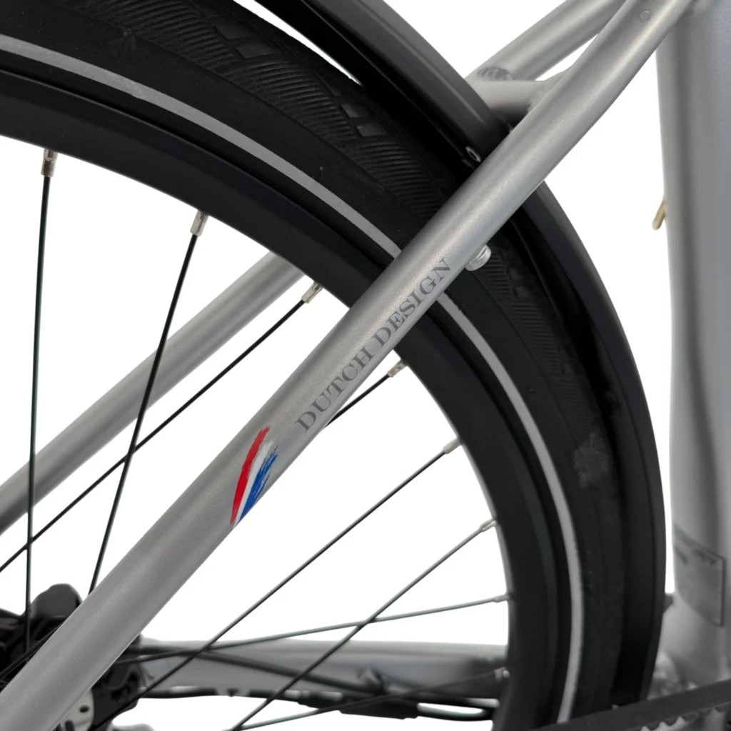 Close-up van een zilveren fietsframe met 'Dutch Design' logo, naast achterband en spatbord.