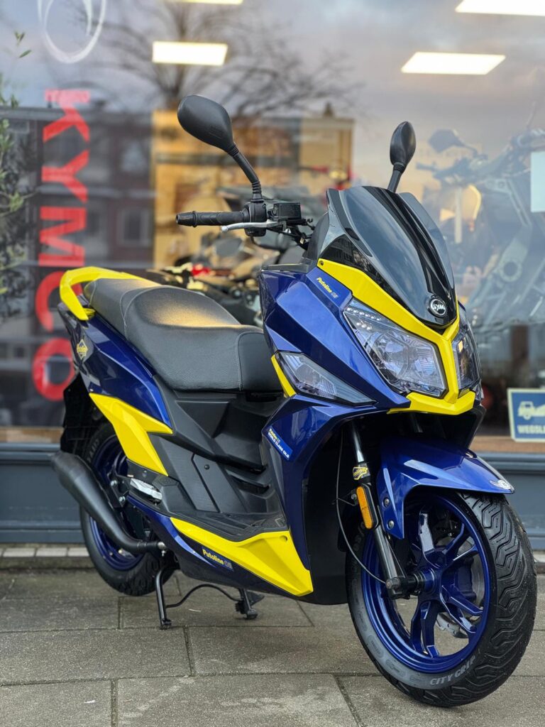 Blauw-gele sportieve scooter geparkeerd voor een winkelpui op de stoep.