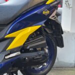 Close-up van blauwe en gele scooter met Putoline-sticker, achterwiel en zadel zichtbaar.