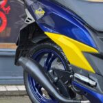 Achterzijde van blauwe-gele scooter met Putoline-sticker, blauwe velg en zwarte uitlaat.