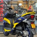 Blauw-gele scooter met Putoline-stickers en Nederlands kenteken, geparkeerd voor een winkelruit