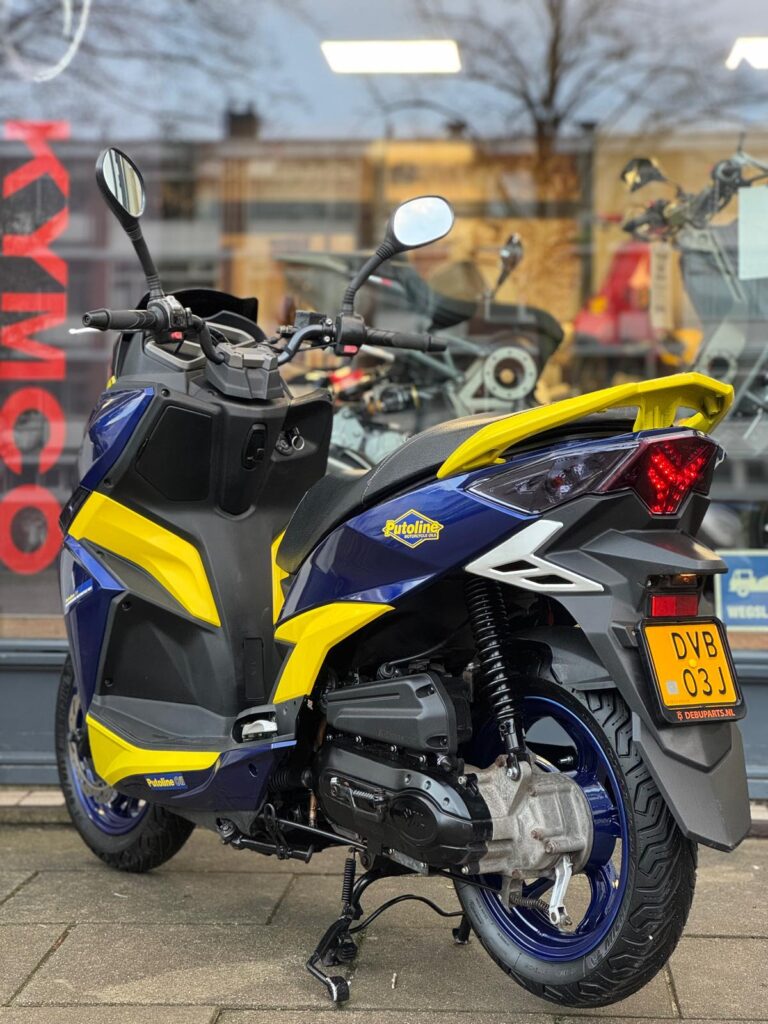 Blauw-gele scooter met Putoline-stickers en Nederlands kenteken, geparkeerd voor een winkelruit
