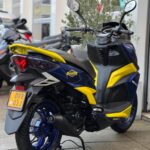 Blauw-gele scooter met Putoline-styling, geparkeerd op de stoep bij een scootershop.