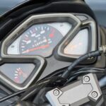 Close-up van het instrumentenpaneel van een scooter met analoge snelheidsmeter, brandstofmeter en stuurklem.