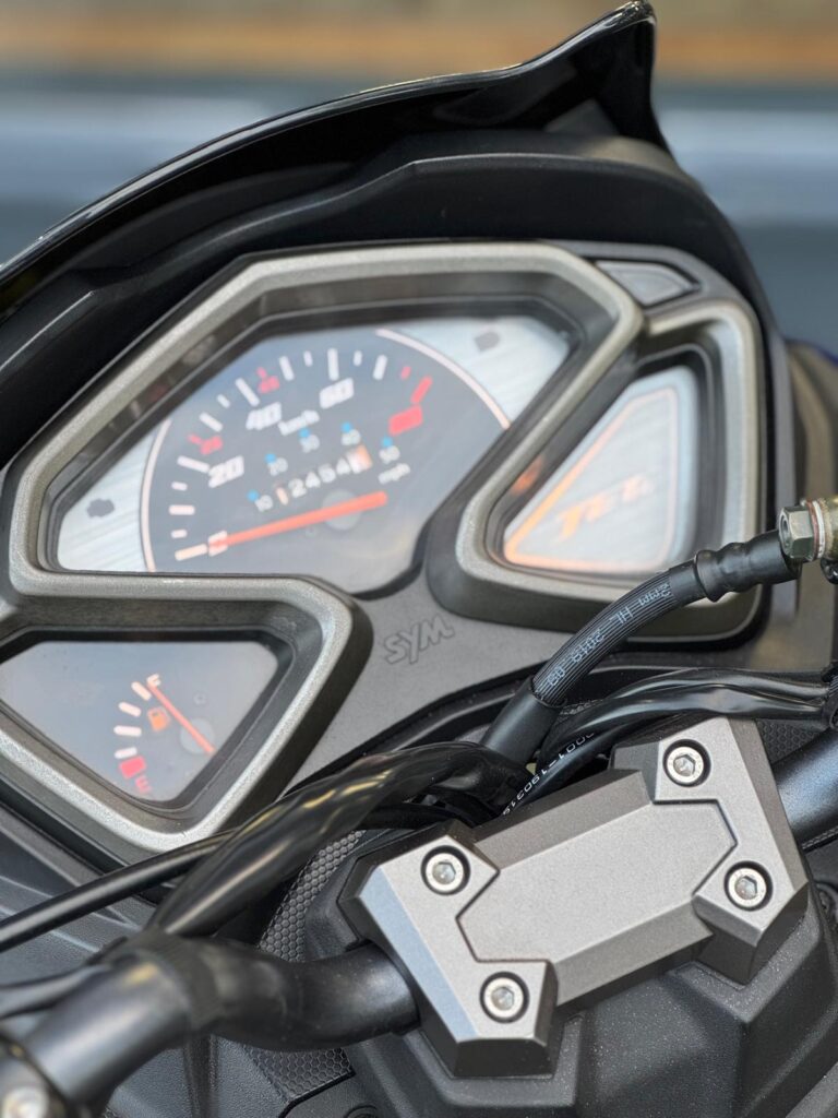 Close-up van het instrumentenpaneel van een scooter met analoge snelheidsmeter, brandstofmeter en stuurklem.