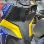 Close-up van stuur en middenconsole van een blauw-gele scooter met contactslot