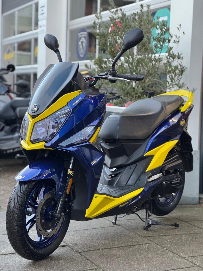 Blauw-gele sportieve scooter met dubbele koplamp, geparkeerd op de stoep bij een showroom.