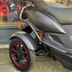 Close-up van het achterwiel en de zijkant van een matte zwarte scooter met rode velgrand en topkoffer.