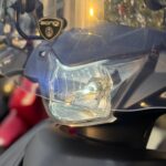 Close-up van scooterkoplamp met windscherm en Biondi-sticker in warm zonlicht