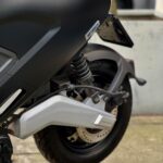 Close-up van de achterzijde van een zwarte elektrische scooter met achterwiel, schokdemper en remschijf.