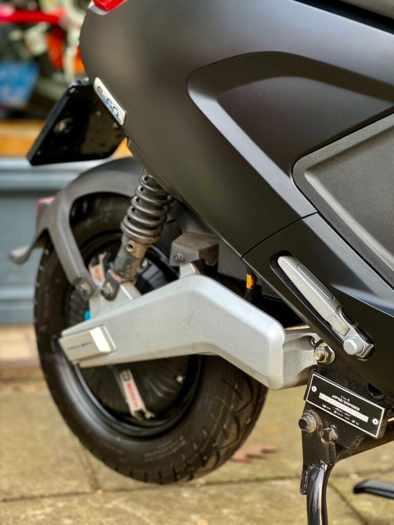 Close-up van het achterwiel, vering en middenbok van een zwarte elektrische scooter.