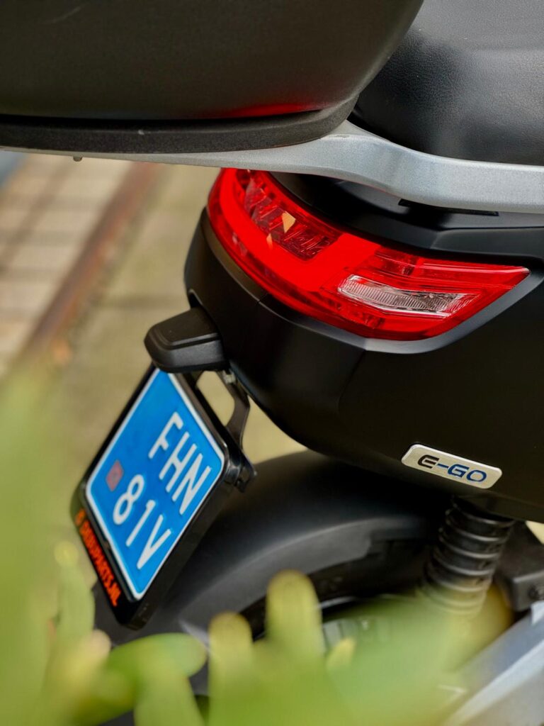 Close-up van de achterzijde van een elektrische scooter met rood achterlicht en blauwe kentekenplaat.