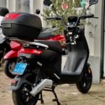 Zwarte elektrische scooter met topkoffer op de standaard voor een winkelpui.