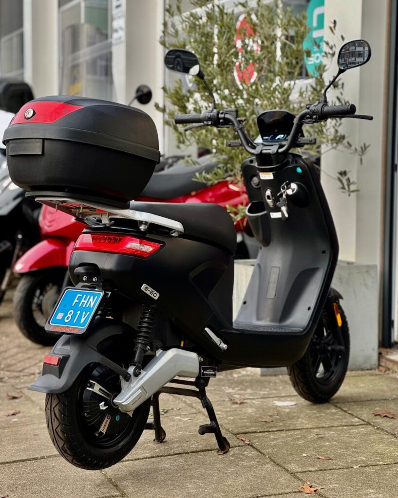Zwarte elektrische scooter met topkoffer op de standaard voor een winkelpui.