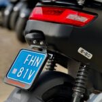 Close-up van de achterzijde van een elektrische scooter met rood achterlicht en blauwe kentekenplaat.