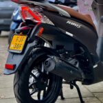 Achterkant van een zwarte scooter met topkoffer, kenteken en rood achterlicht op de stoep.