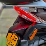 Close-up van de achterzijde van een scooter met rood achterlicht, reflector en gele kentekenplaat.