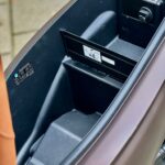 Lege opbergruimte onder het zadel van een scooter, met uitklapbare vakverdeler en waarschuwingsstickers.