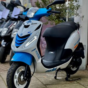 Blauw-witte scooter op standaard voor een winkel, met andere scooters op de achtergrond.