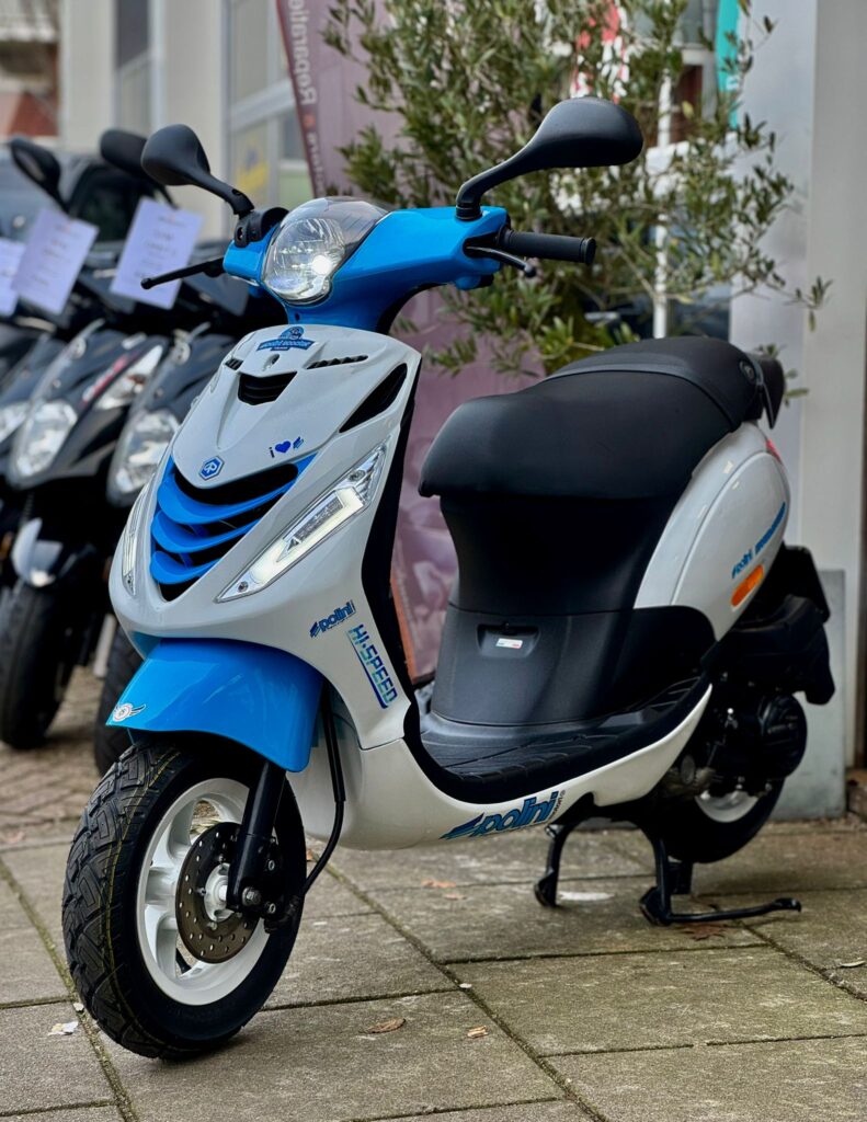 Blauw-witte scooter op standaard voor een winkel, met andere scooters op de achtergrond.