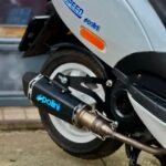 Detail van achterwiel en Polini sportuitlaat op grijze scooter, geparkeerd buiten.