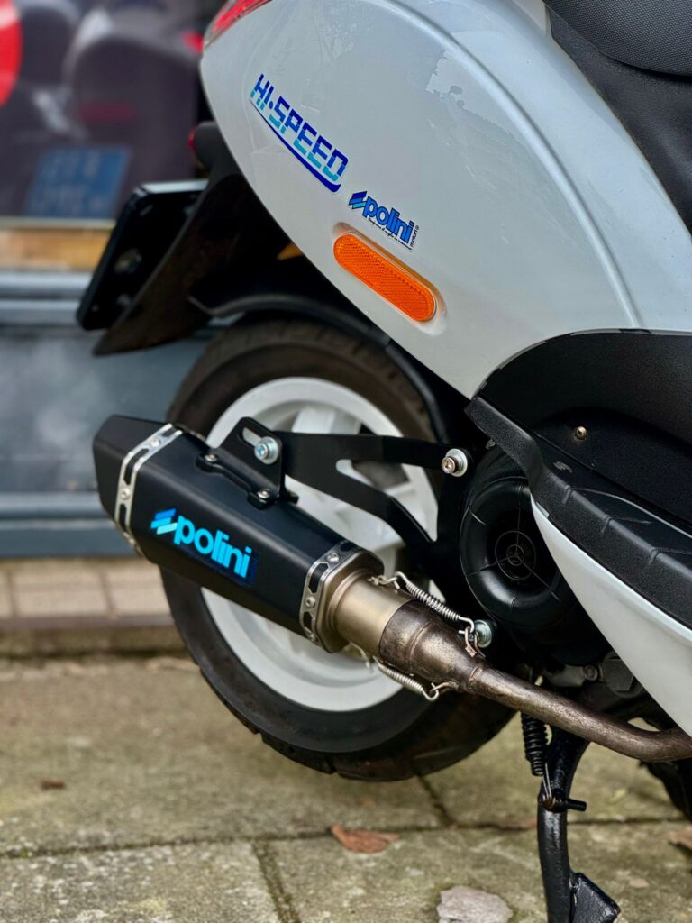 Detail van achterwiel en Polini sportuitlaat op grijze scooter, geparkeerd buiten.