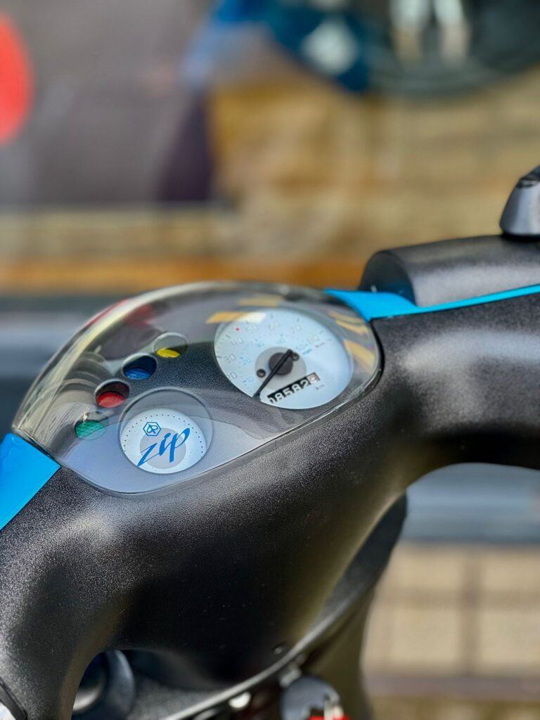 Close-up van het dashboard van een scooter met snelheidsmeter, kilometerteller en controlelampjes.