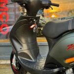 Close-up van een zwarte scooter met sleutel in het contact, bij zonsondergang voor een etalage.