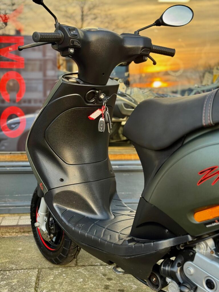 Close-up van een zwarte scooter met sleutel in het contact, bij zonsondergang voor een etalage.