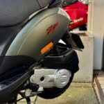 Close-up van een Piaggio Zip scooter, zijkant met zadel en motorblok, buiten geparkeerd.