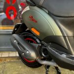 Close-up van de achterkant van een matgroene scooter met zwart zadel, uitlaat en rood wielaccent.