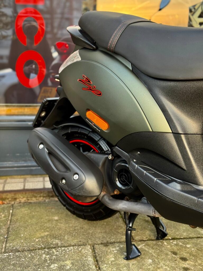Close-up van de achterkant van een matgroene scooter met zwart zadel, uitlaat en rood wielaccent.