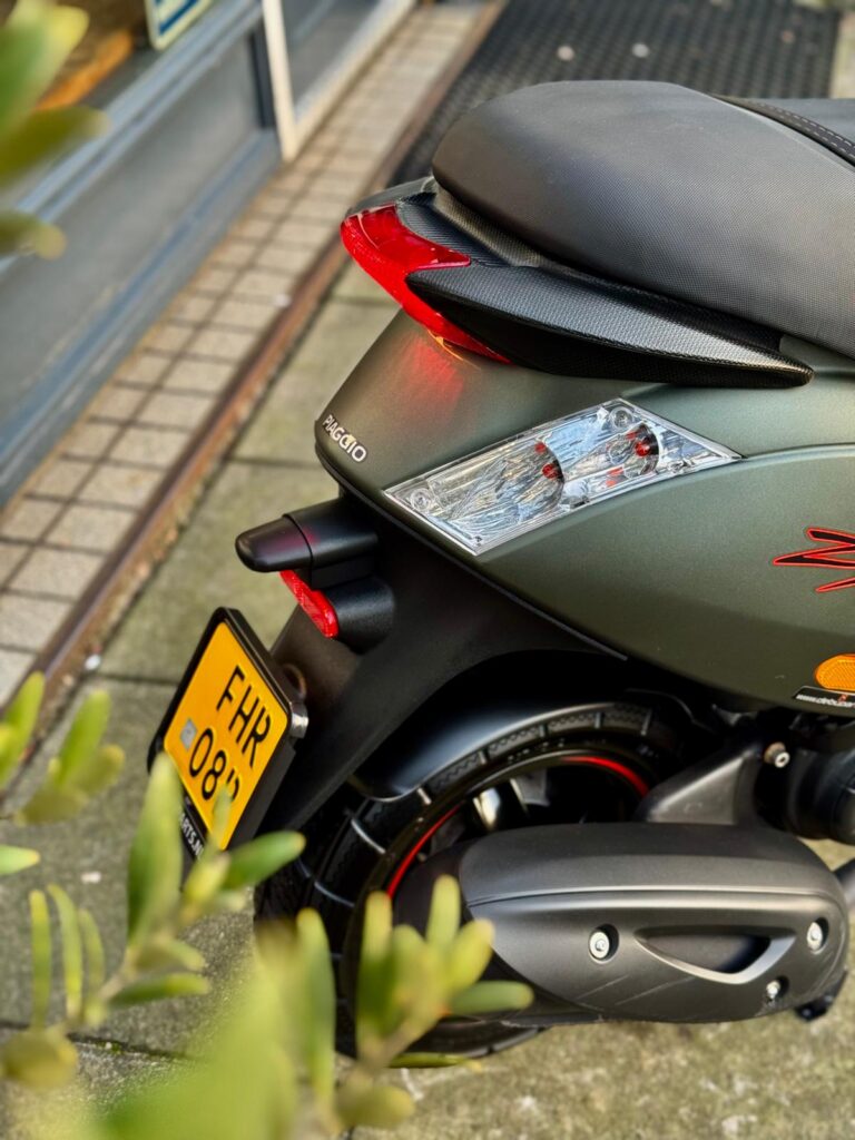 Close-up van de achterkant van een groene Piaggio-scooter met rood achterlicht en kenteken.