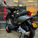 Donkergroene Piaggio-scooter op standaard voor een winkelraam bij zonsondergang.