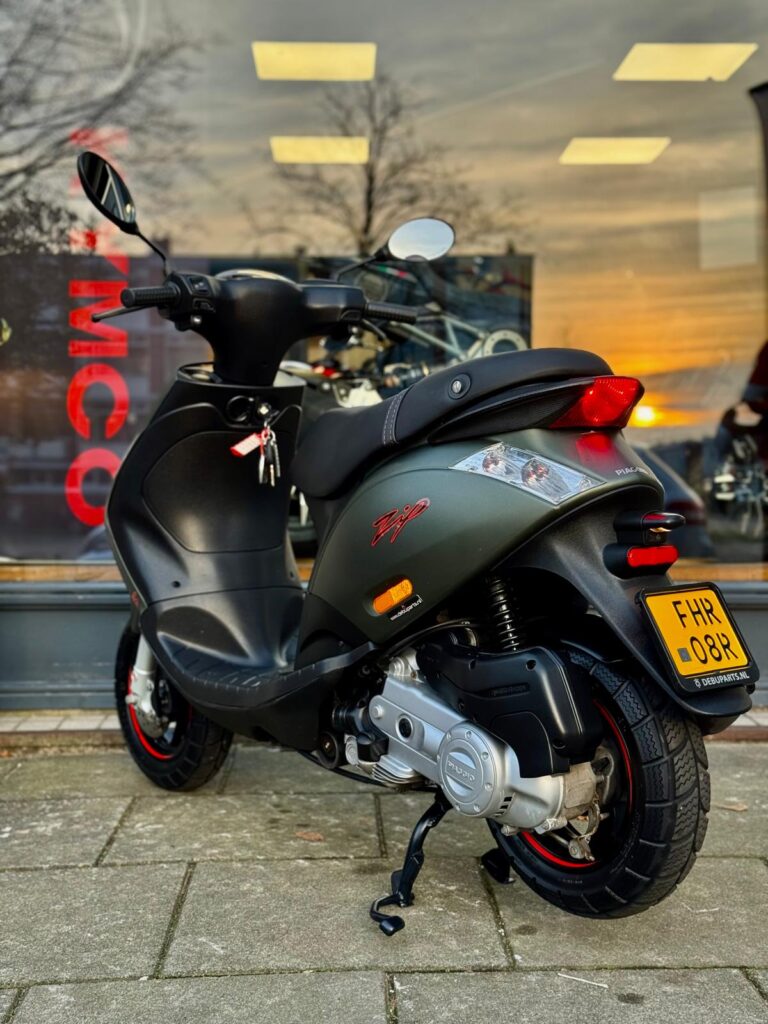 Donkergroene Piaggio-scooter op standaard voor een winkelraam bij zonsondergang.