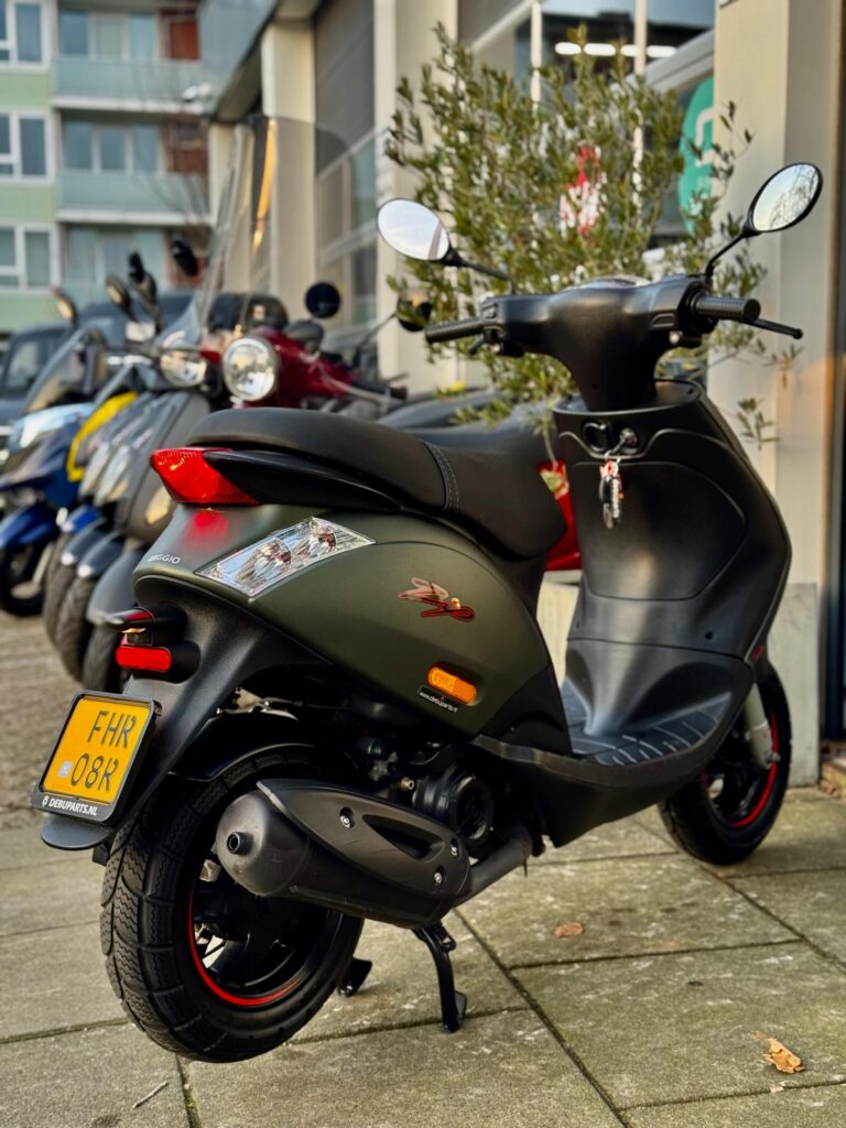 Groen-zwarte scooter met rode accenten geparkeerd voor een scootershop op de stoep.