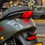 Close-up van de achterzijde van een Piaggio-scooter met rood achterlicht, knipperlichten en gele kentekenplaat.